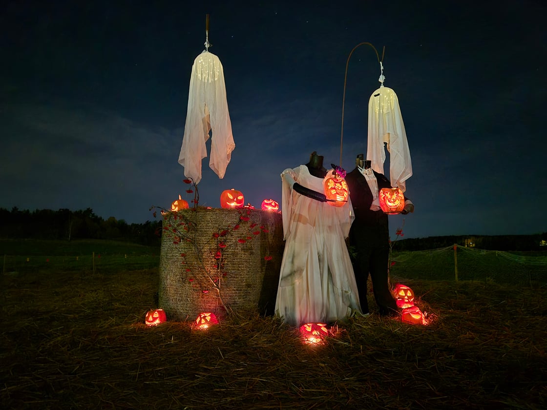 Päätön hääparihahmo kurpitsapuistossa kurpitsalyhtyjen loisteessa pimeässä.